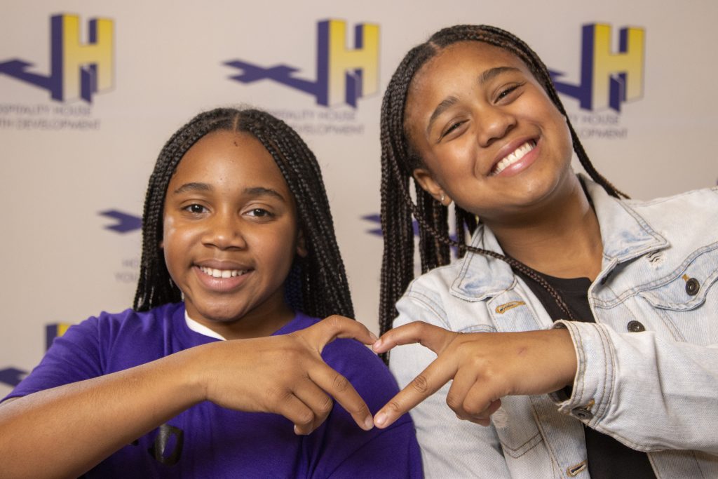 Two young ladies, using their hands to create a heart symbol.